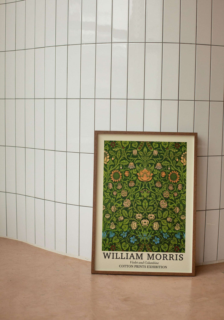 Beyaz dikey seramik duvar önünde yerde duran, ahşap çerçeveli William Morris Larkspur 1875 botanik desenli sergi posteri